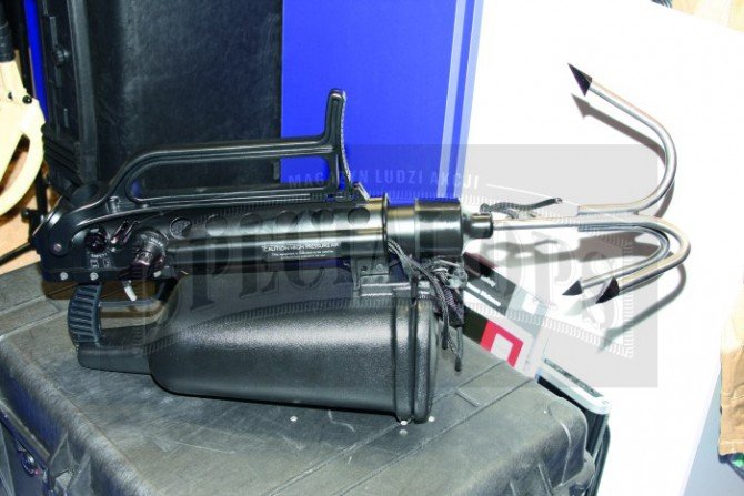 Assault Launcher Max z kolbą złożoną na grzbiet urządzenia. Widoczny pojemnik na linę lub nylonową drabinkę.