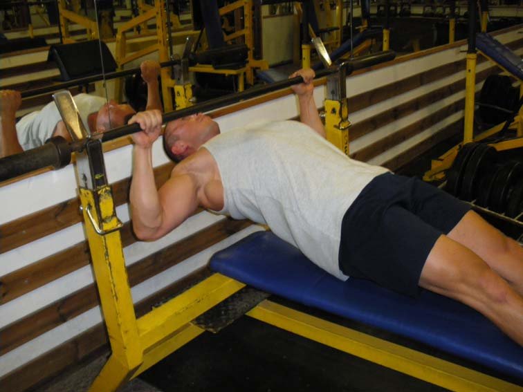 Podciąganie tułowia do gryfu sztangi w pozycji poziomej – doskonałe ćwiczenie z wykorzystaniem masy ciała do rozwoju mięśni najszerszych grzbietu wykonuje Rafał Osiński (siłownia TKKF Syrenka w Warszawie).