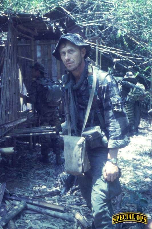 Sierż. Slugocki podczas patrolu na szlaku Ho Chi Minha na pograniczu z Laosem, 10 dni drogi od Dak Pek, kwiecień 1967 r. Ma na sobie popularny w Siłach Specjalnych mundur w kamuflażu Tiger Stripe z kapeluszem dżunglowym oraz oporządzenie M1956 LCE, uzbro.