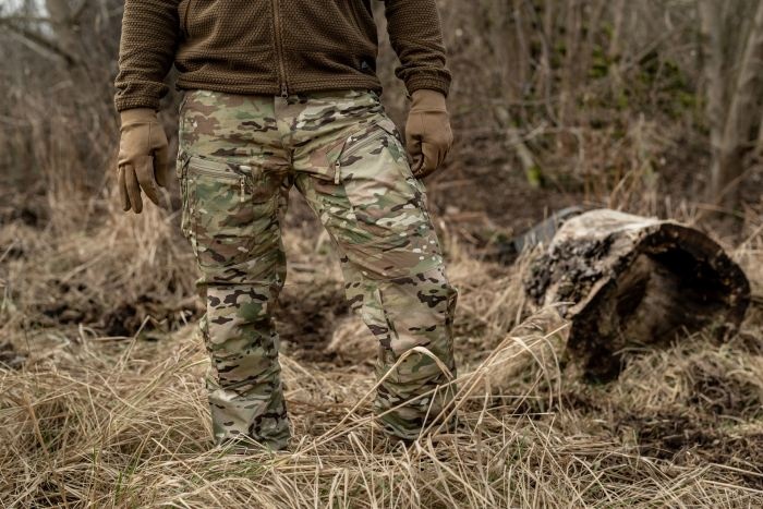 mężczyzna w spodniach multicam na suchej trawie