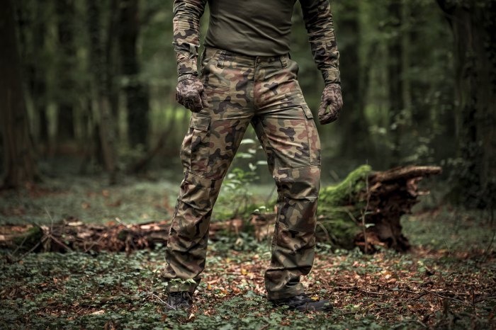 mężczyzna od pasa w dół w spodniach multicam w lesie